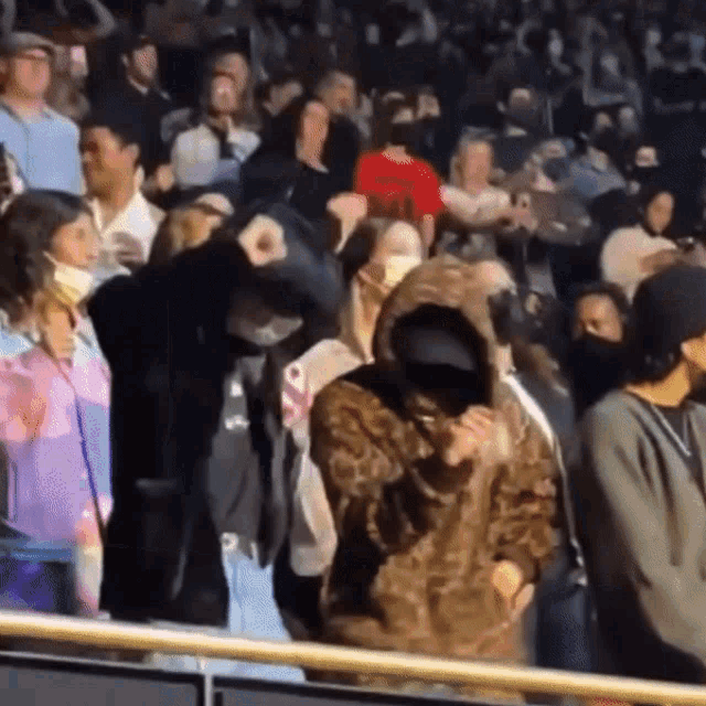 a woman in a leopard print hoodie stands in a crowd of people wearing face masks