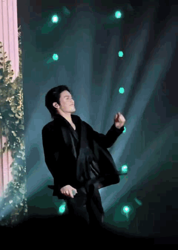 a man in a suit is dancing on a stage with green lights behind him