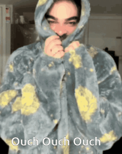 A person in a paint-splattered hoodie covers their mouth with “Ouch Ouch Ouch” text.
