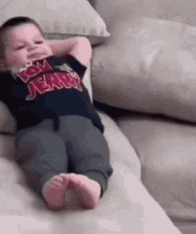 A small baby reclines against a sofa cushion, looking relaxed.