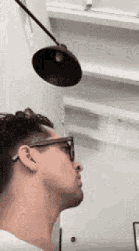 a man wearing glasses is looking up at a lamp .