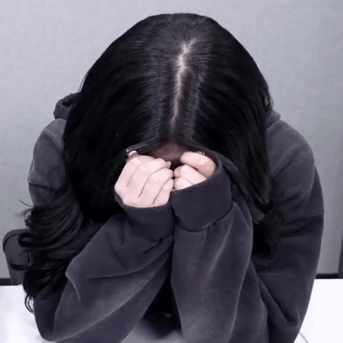 A person bows forward and covers their face in an apologetic pose.