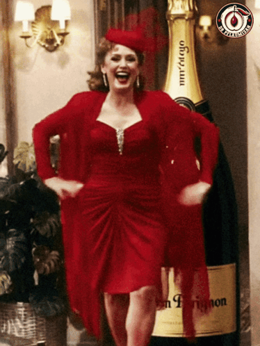 a woman in a red dress standing next to a bottle of champagne