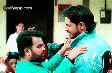 two men are hugging each other in a room with a crowd behind them .
