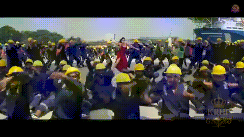 a woman in a red dress is dancing in front of a large group of construction workers wearing hard hats