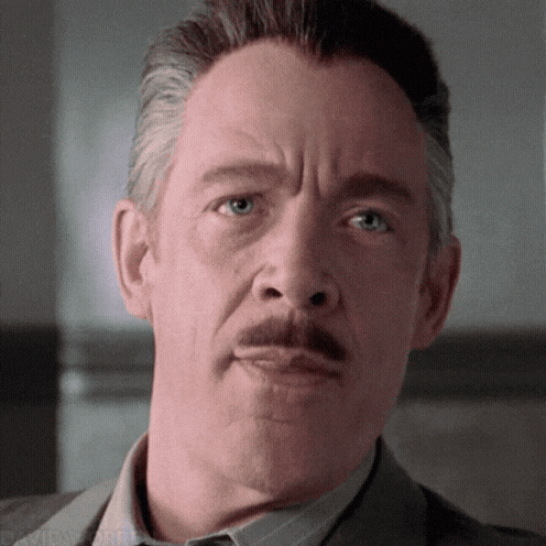 A mustached man looks forward with a restrained, serious expression.
