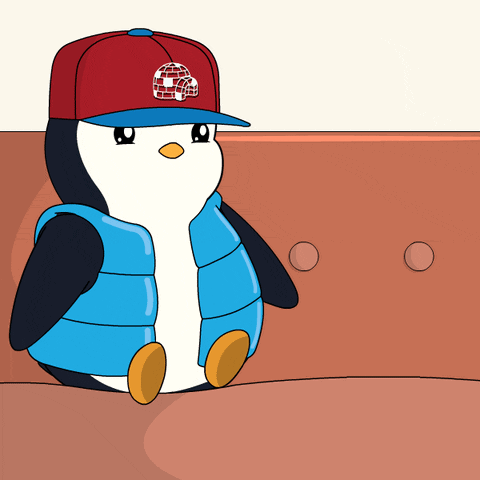 A blue penguin in a red cap and vest looks tired on a train seat.