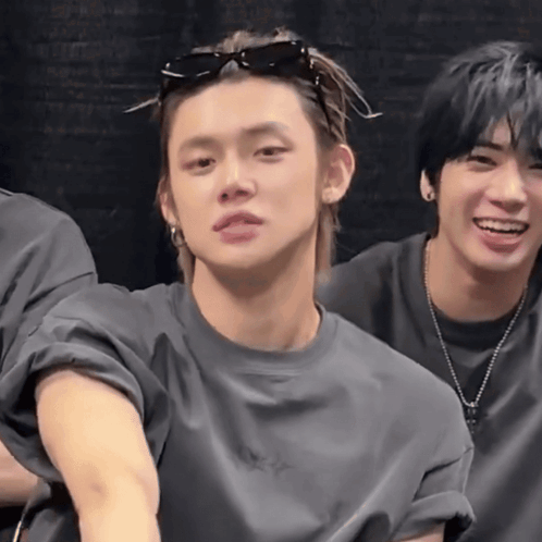 a man wearing sunglasses looks at the camera while another man laughs in the background