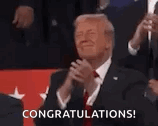 donald trump is applauding while wearing a suit and tie and holding a microphone .