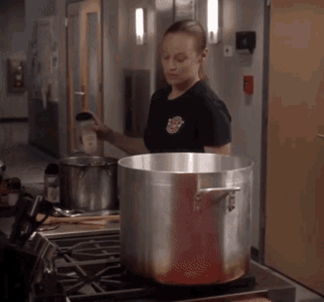 a woman in a fireman 's shirt is pouring something into a pot