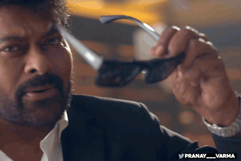 a man in a suit is holding a pair of sunglasses with the hashtag pranay_varma at the bottom