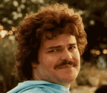 A mustached man gives a small, uneasy smile.