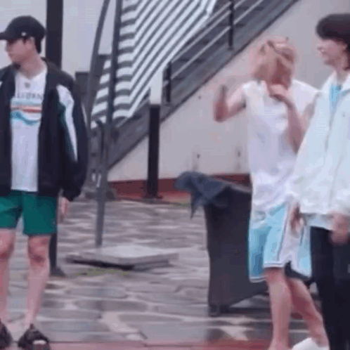 a group of young men are standing on a wet sidewalk .
