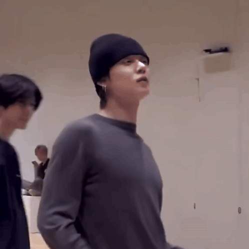 a man wearing a black beanie and a gray sweater is standing in a room .