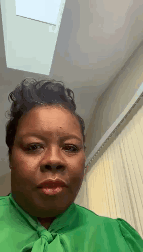 A woman in a green shirt looks forward in disbelief.