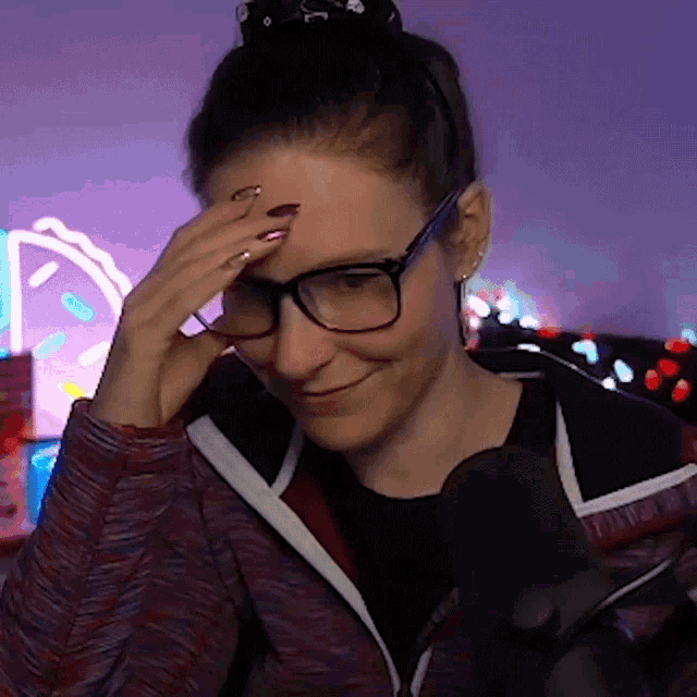 Woman wearing glasses awkwardly smiles and shields her face with her hand.