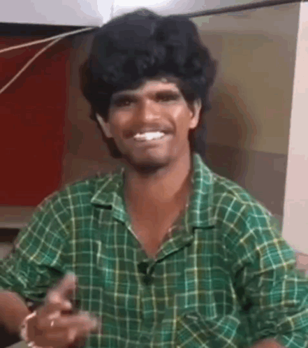 A smiling man in a green plaid shirt gestures enthusiastically.