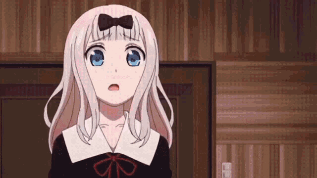 a girl with white hair and blue eyes is standing in a room with a bow on her head .