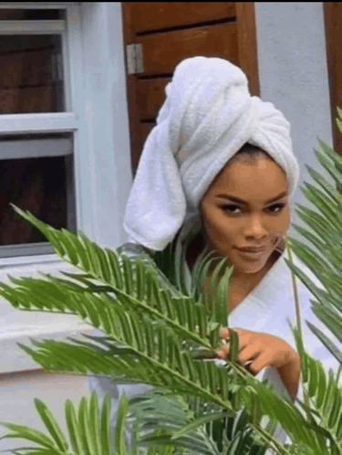 a woman with a towel wrapped around her head is peeking out from behind a plant .