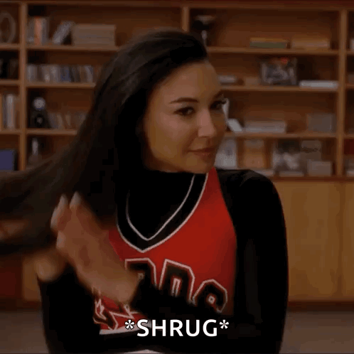 a woman in a cheerleader uniform is holding her hair in a room with a bookshelf in the background .