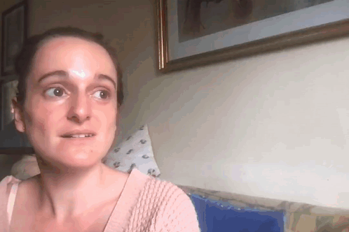 a woman in a pink sweater is sitting on a couch in front of a picture on the wall .