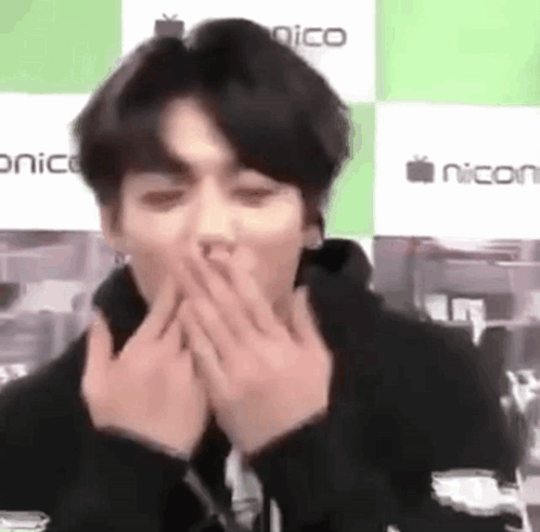 Jungkook covers his mouth with both hands in a blurry close-up.