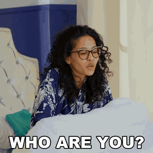 a woman with curly hair and glasses is laying on a bed with the words who are you below her