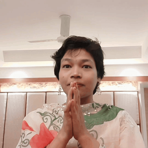 a woman with her hands folded in front of her face and a ceiling fan in the background