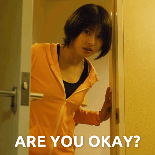 a woman in an orange jacket is standing in a doorway with the words are you okay below her