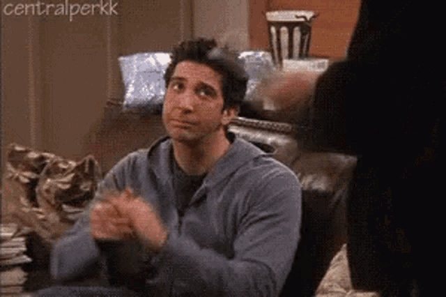 Joey Tribbiani claps while holding a cat in a Central Perk scene.