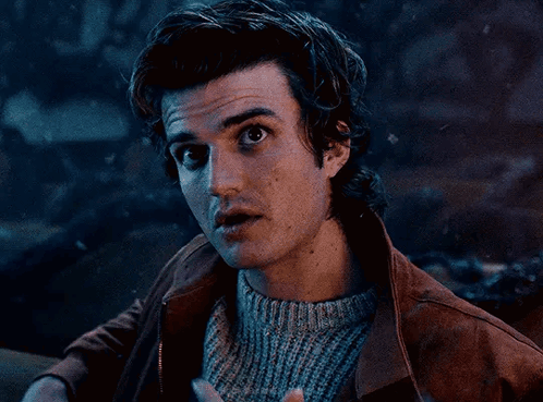 a young man wearing a sweater and a brown jacket is talking to someone .