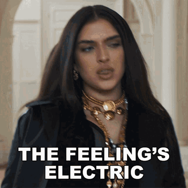 a woman in a black jacket and gold necklace says " the feeling 's electric " in white letters