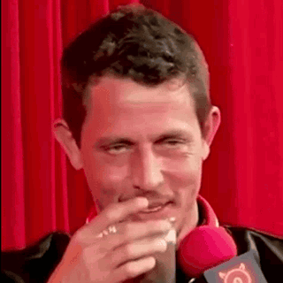 a man is sitting in front of a red curtain drinking a drink .