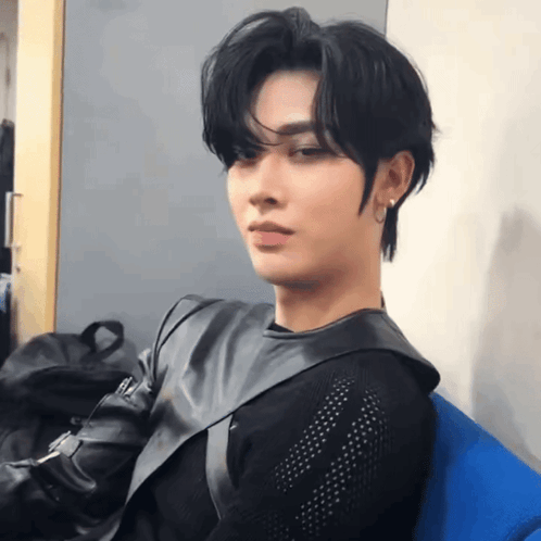 a young man is sitting on a blue chair wearing a black jacket