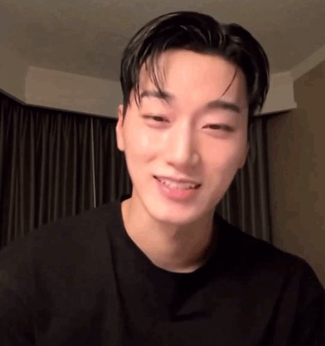a young man in a black shirt is smiling and looking at the camera in a room .