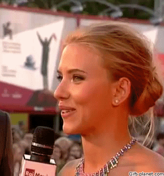 A blonde woman smiles and winks while being interviewed with a microphone.
