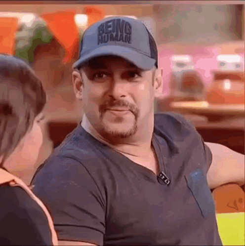 a man wearing a baseball cap and a black shirt is sitting at a table talking to a woman .