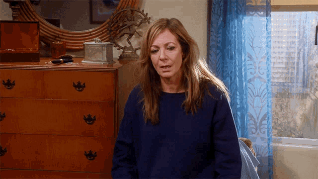 a woman in a blue sweater is sitting in front of a wooden dresser