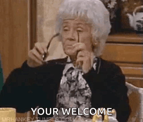 An older woman in a dark cardigan holds up her glasses, captioned ‘YOUR WELCOME’.
