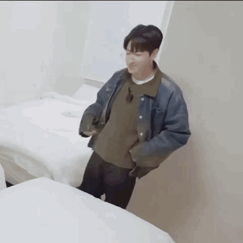 Jungkook stands in a bright room wearing layered casual clothes.