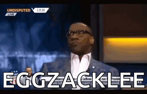 a man in a suit and glasses says eggzacklee on a television show .