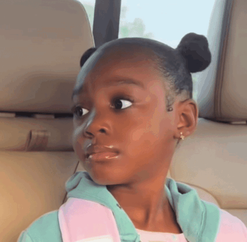 a little girl is sitting in the back seat of a car looking at the camera