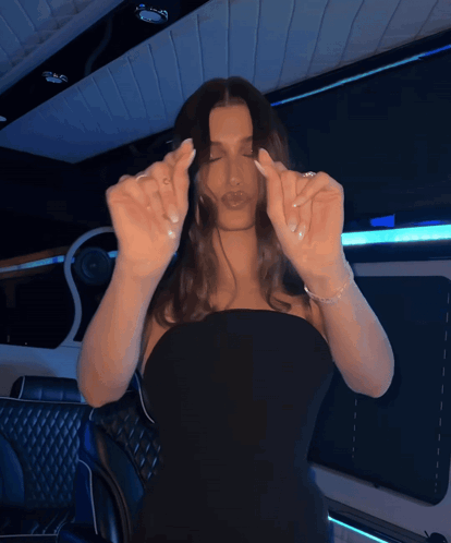Woman in a black dress raises her hands near her face in a blue-lit room.