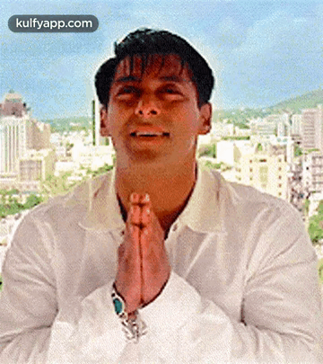 a man in a white shirt is praying with his hands folded in front of a city skyline .