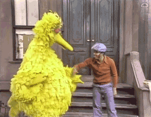 Big Bird reaches toward another Sesame Street character for a high five.