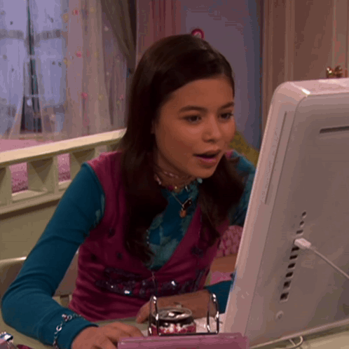 a girl is sitting at a desk looking at a computer screen