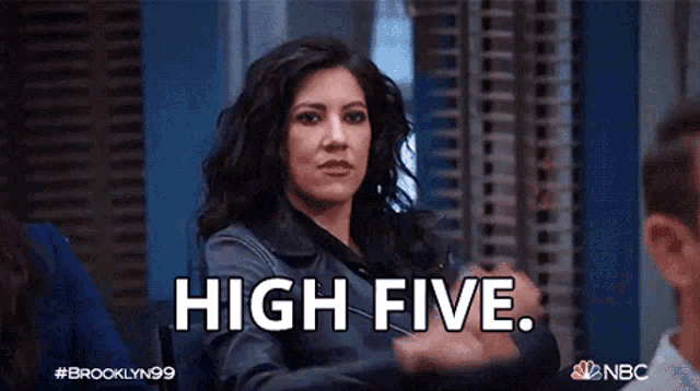 Woman raises one hand for a high five in an office setting.