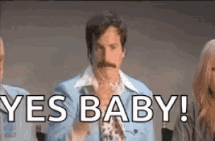 a man in a blue suit is standing in front of a group of people and saying yes baby .