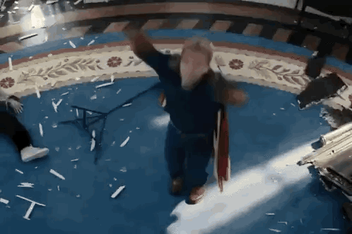 a man in a blue shirt is dancing in a room with broken glass