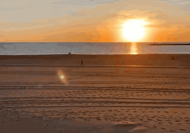 a person walking on a beach at sunset with the sun shining through the clouds